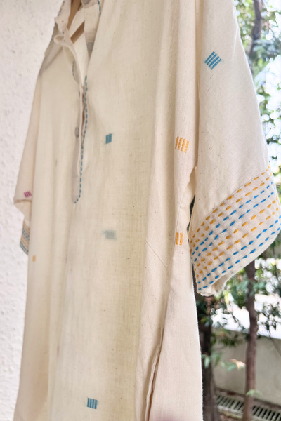 Cream fabric with colorful squares and embroidered half sleeves hanging against a light background